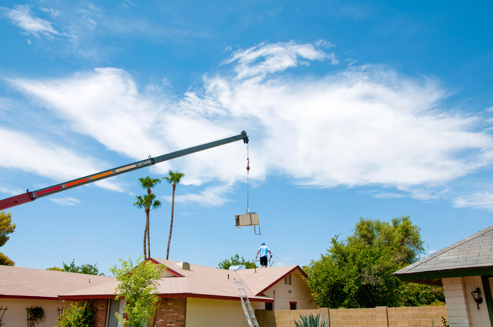 Image of an Air Conditioner being lifted by a crane with a worker